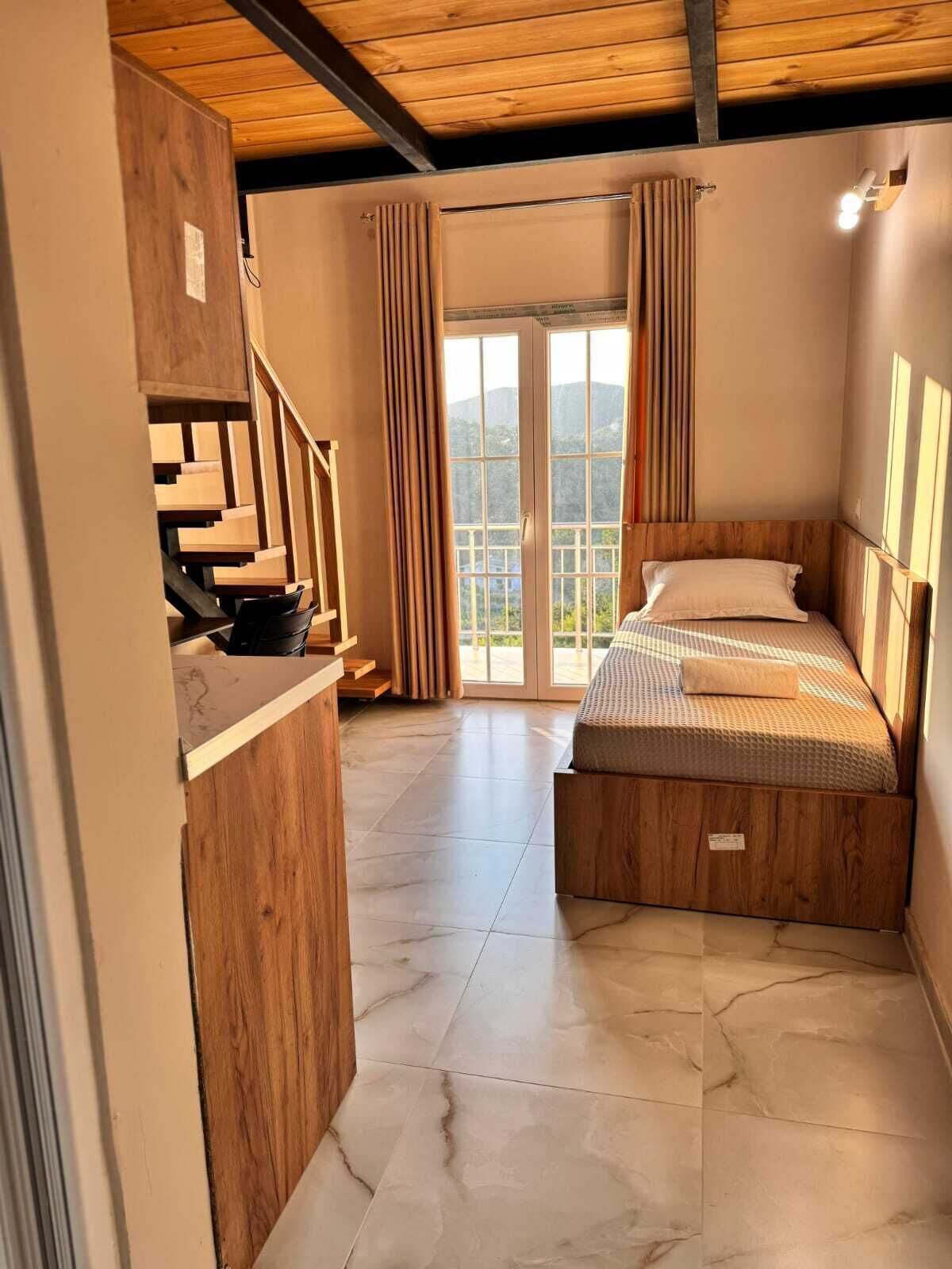Ein Schlafzimmer mit Bett, Holz-Kopfteil, Vorhängen und Blick durch eine Glastür.