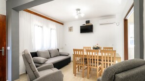 Ein modernes Wohnzimmer mit einer Couch, Sesseln, einem Fernseher und einem Esstisch.