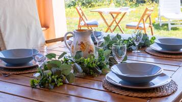 Une table en bois, dressée pour le repas, avec des bols, des verres et une carafe, le tout entouré de verdure.