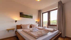 Ein Doppelbett mit Holz-Kopfteil, zwei Nachttische, ein Gemälde an der Wand und ein Fenster mit Vorhängen.