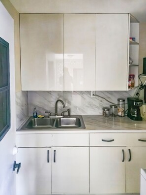 A kitchen with a double sink, white cabinets, and a coffee maker on the countertop. - Efficiency Apartment Studio - Port St. Lucie (Port St. Lucie)