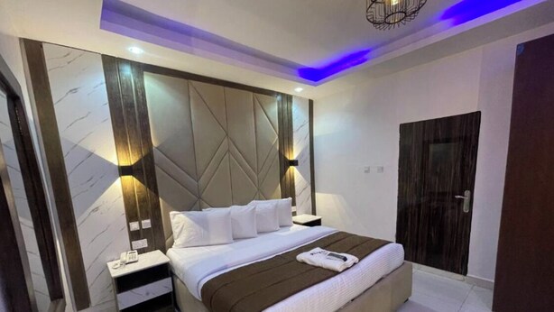 A modern hotel room with a large bed, two bedside tables, a nightstand, and a built-in headboard. - Presken Hotel Signature (Lagos)
