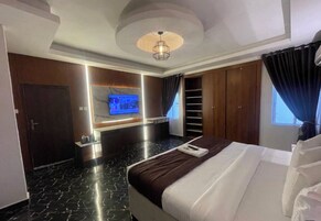 Una habitación de hotel moderna con una cama grande, un televisor de pantalla plana montado en la pared, un armario empotrado y una lámpara en el techo.