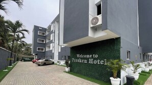 A hotel entrance with a paved driveway, a sign reading 'Welcome to Presken Hotel,' and a row of potted plants along the walkway. - Presken Hotel Signature (Lagos)