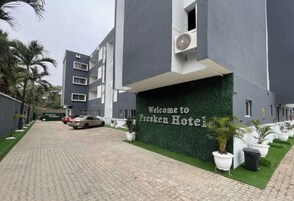 La entrada de un hotel con un camino pavimentado, un letrero que dice 'Welcome to Presken Hotel' y una fila de macetas con plantas a lo largo del sendero.