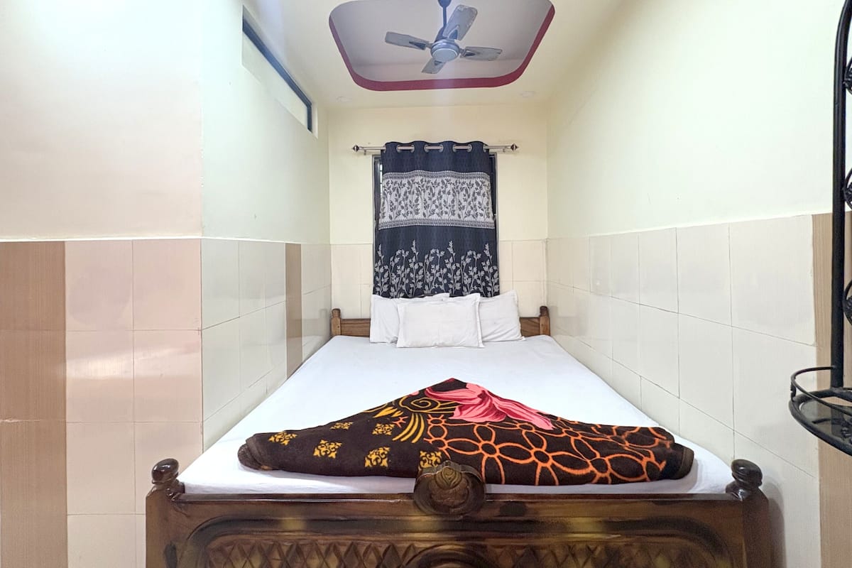 A single bed with a wooden headboard, a ceiling fan, a patterned curtain, and a tiled wall.