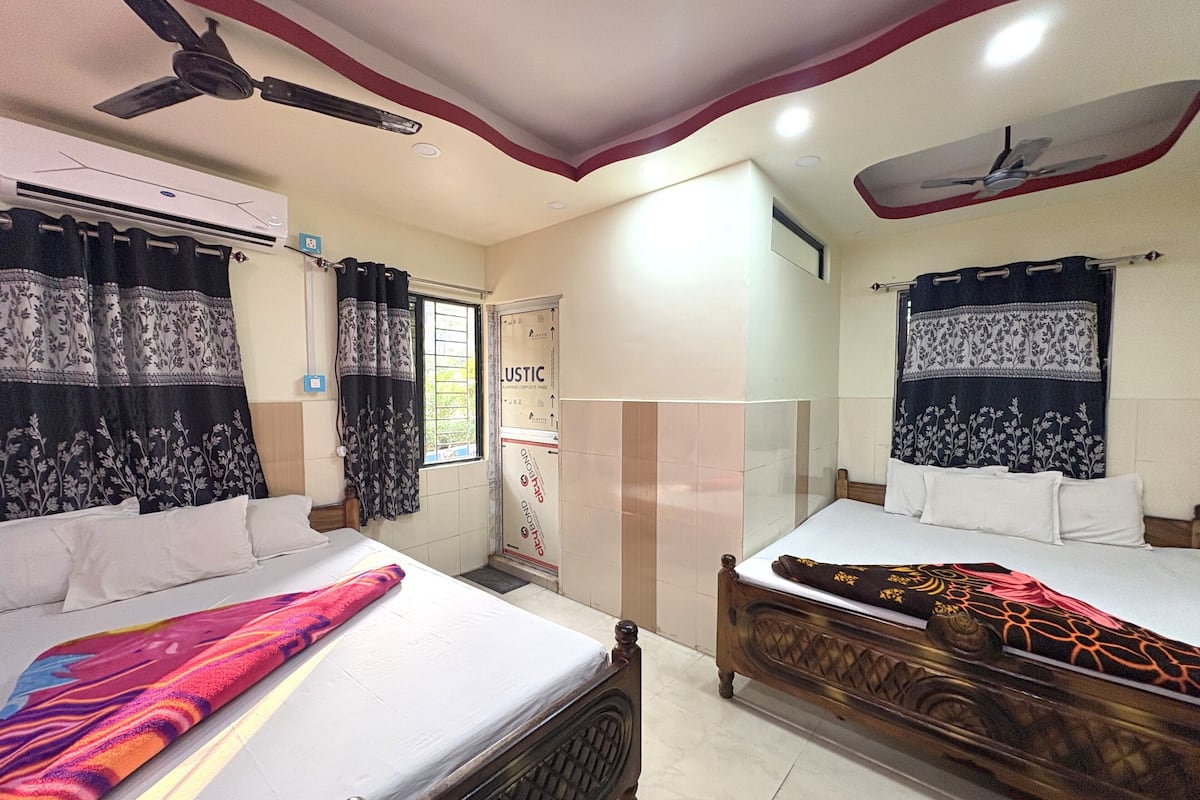 A hotel room with two beds, a ceiling fan, an air conditioning unit, and a window with curtains.