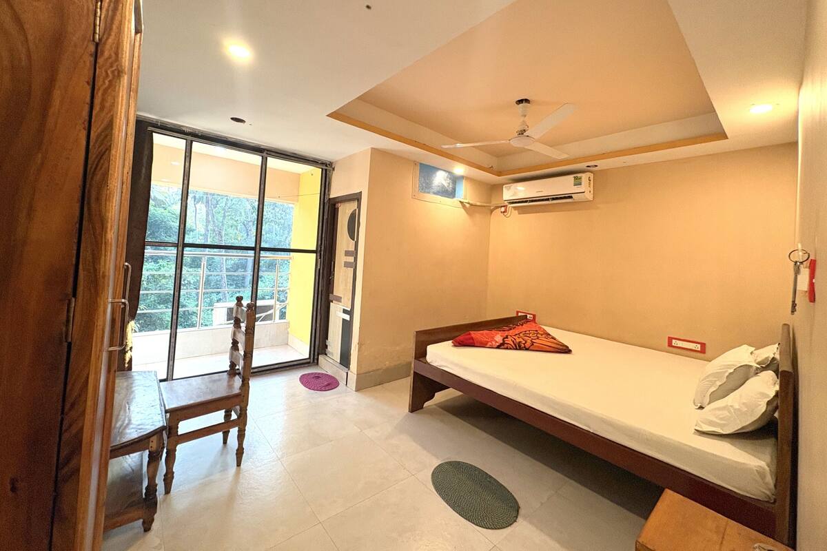 A bedroom with a bed, a desk, a chair, a window, and an air conditioning unit.