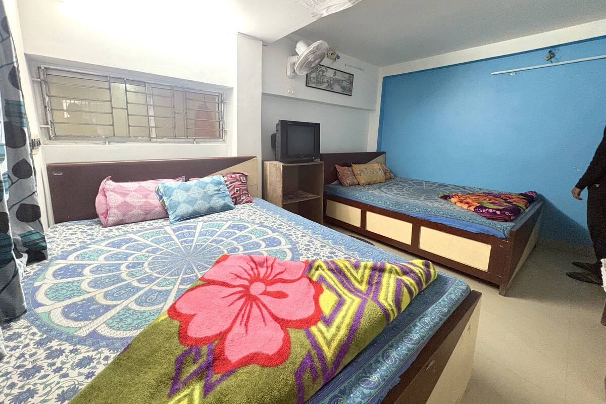 A bedroom with a bed, a TV, a small desk, and a window with bars.