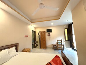 A hotel room with a bed, a wooden wardrobe, a television mounted on the wall, a chair, and a window. - Old Digha Hotel Swastika Inn  (Digha)