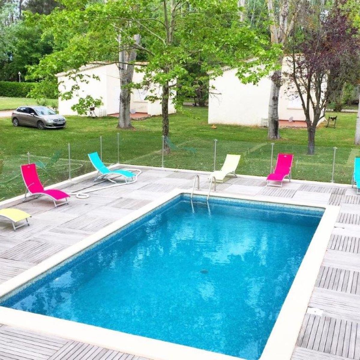 A rectangular swimming pool with a wooden deck and colorful lounge chairs.