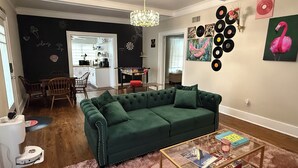 A living room with a green sofa, a coffee table, and a wall decorated with vinyl records and a flamingo painting. - Biscayne Hideaway- 3 bed house Miami Big Yard Driveway - Downtown/Wynwood - FIFA (Miami)