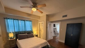 A bedroom with a bed, a ceiling fan, a nightstand with a lamp, a wardrobe, and a view of a hallway leading to a bathroom. - Biscayne Hideaway- 3 bed house Miami Big Yard Driveway - Downtown/Wynwood - FIFA (Miami)