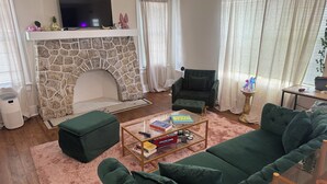 A living room with a stone fireplace, a green sofa, a coffee table with books, and a television on a white mantelpiece. - Biscayne Hideaway- 3 bed house Miami Big Yard Driveway - Downtown/Wynwood - FIFA (Miami)