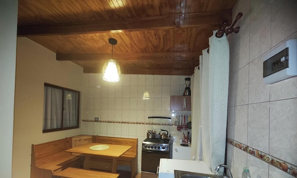 Eine Küche mit Holzbalkendecke, weißen Fliesenwänden, einem Holztisch und einem Herd.