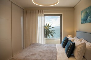 A hotel room with a bed, curtains, a painting, and a view of the sea. - GET Seaside Vibe Apartments Loutraki (Loutraki)