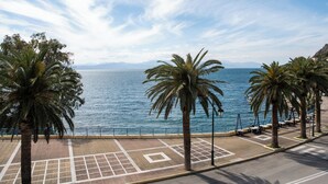 Eine Uferpromenade mit Palmen, wolkenlosem Himmel und Blick auf das Meer.