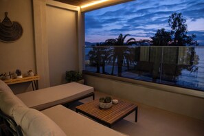 A balcony with a view of palm trees and a sunset, a sofa, a small table with a plant, and a wall-mounted decorative item. - GET Seaside Vibe Apartments Loutraki (Loutraki)