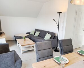 A modern living room with a grey sofa, a wooden coffee table, and a floor lamp. - Exclusive Seepark Suite vacation apartment in Nordhorn. Child-friendly furnishings with 2 balconies and plenty of modern entertainment electronics. Wellness area with sauna, wellness shower & whirlpool (Nordhorn)