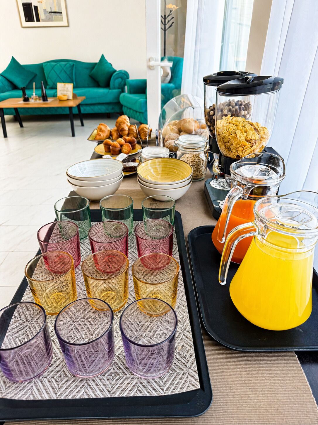 A breakfast buffet with various food items and drinks, a coffee maker, and a green couch in the background.