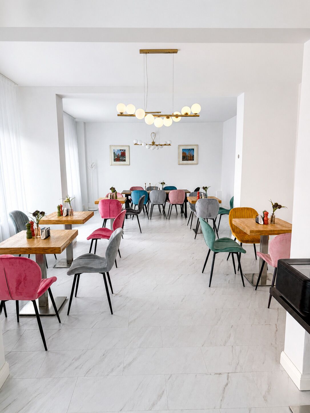 Un comedor moderno con varias mesas y sillas, una araña y cuadros en la pared.