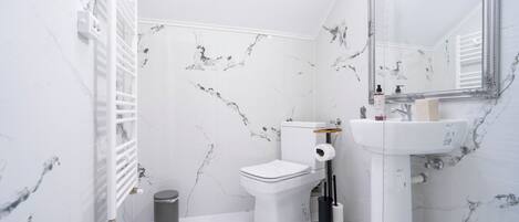 A bathroom with a toilet, sink, mirror, and marble-patterned walls.