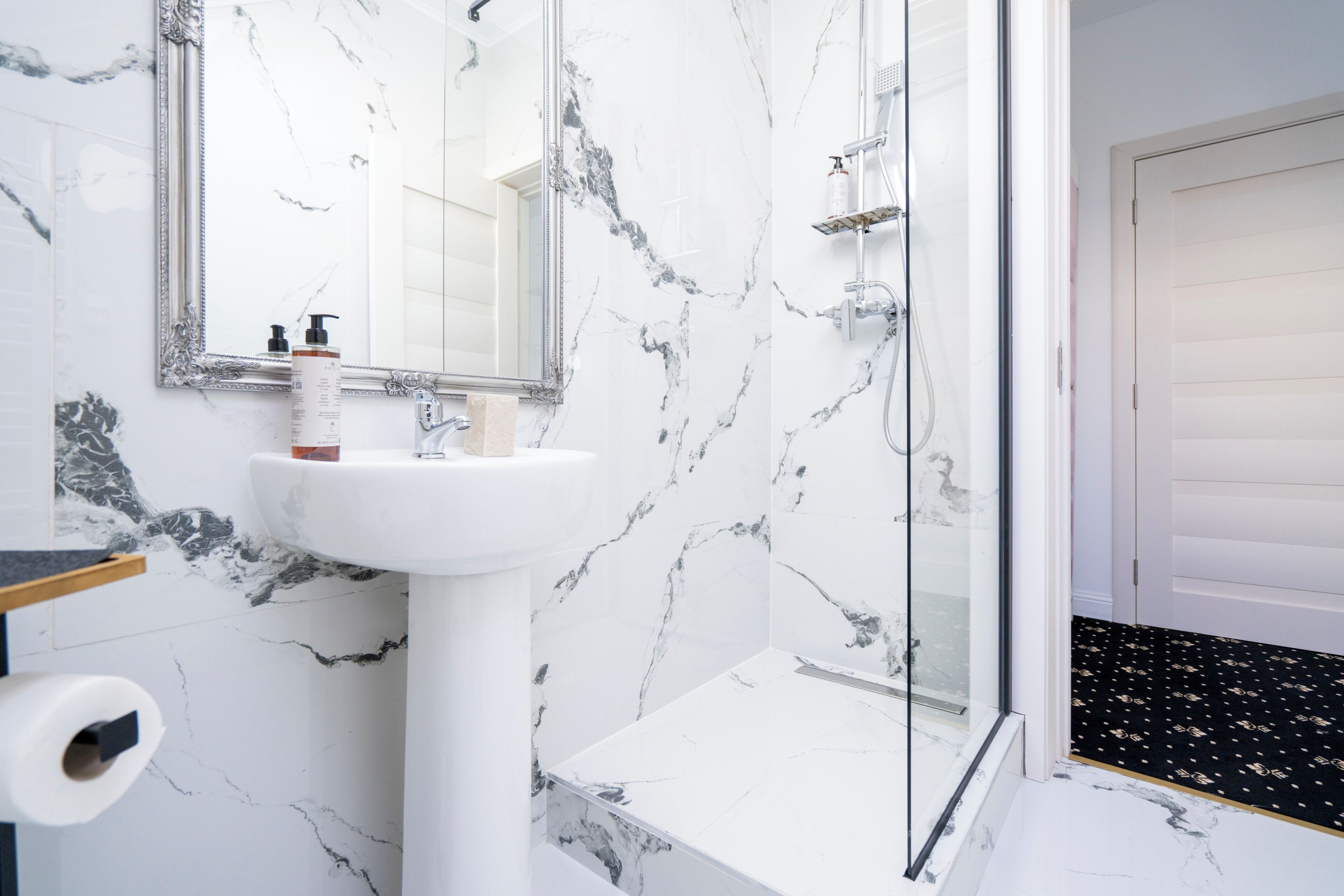 A bathroom with a marble sink, a mirror, a shower, and a toilet paper holder.