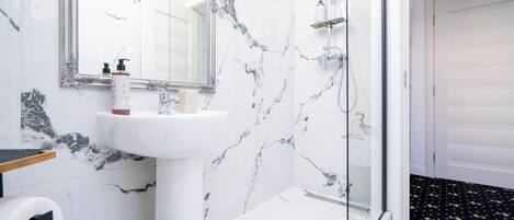 A bathroom with a marble sink, a mirror, a shower, and a toilet paper holder.