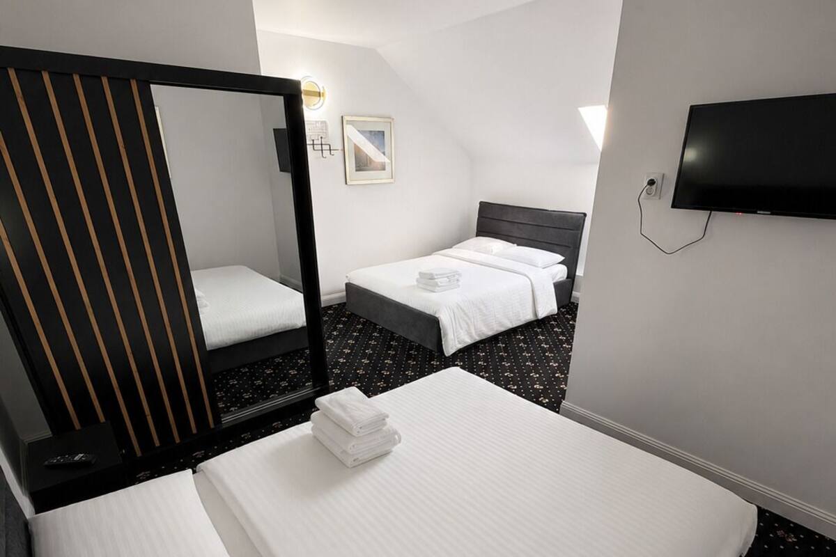 Una habitación de hotel con dos camas, un espejo grande, un televisor de pantalla plana y un televisor instalado en la pared.