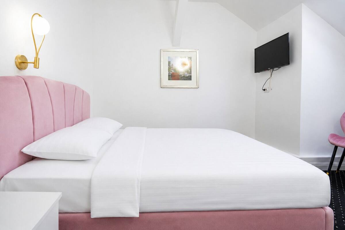 Un dormitorio con cama, televisor de pared, un cuadro enmarcado y un diseño de techo original.