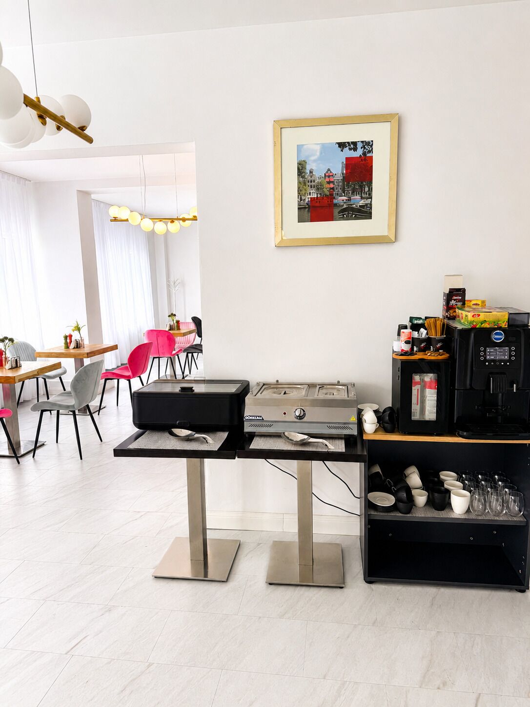A modern kitchen with a coffee machine, a dining area with chairs, and a framed picture on the wall.
