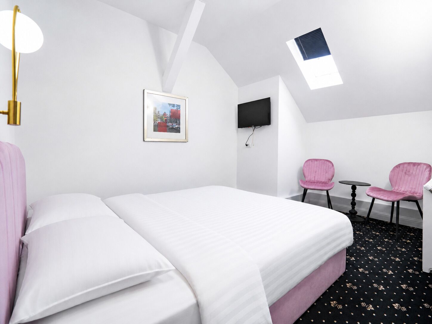 Habitación de hotel con cama, escritorio, dos sillas, televisor y un cuadro en la pared.