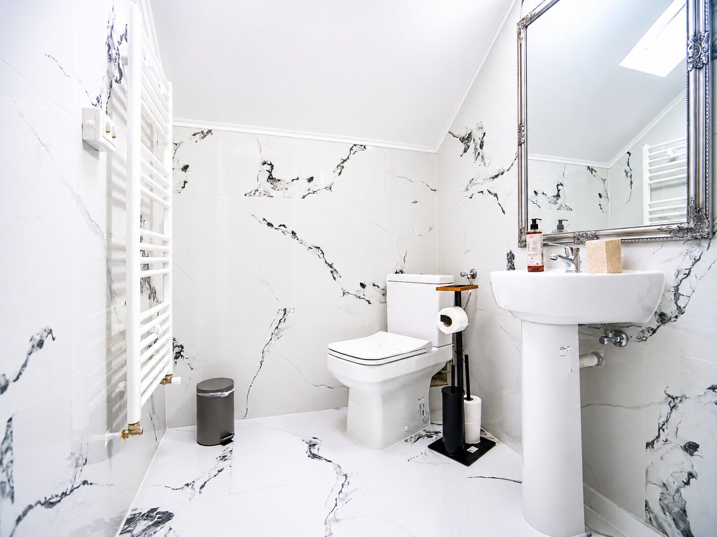 Un baño con inodoro, lavamanos, espejo y paredes con diseño de mármol.
