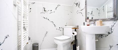 Un baño con inodoro, lavamanos, espejo y paredes con diseño de mármol.