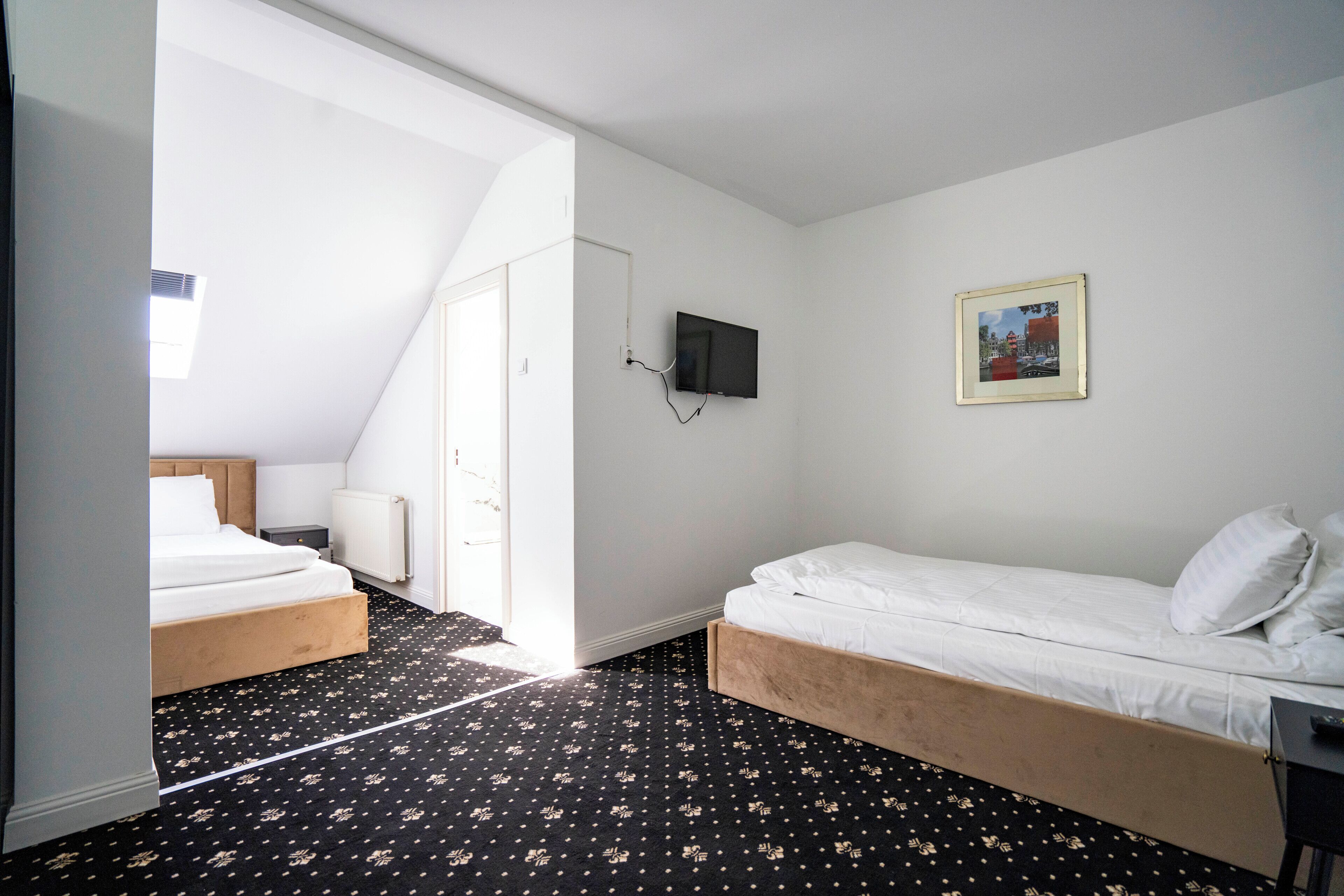 Habitación de hotel con dos camas, un televisor montado en la pared, un cuadro enmarcado y una alfombra estampada.