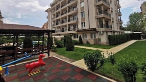 A multi-story residential building with balconies, a paved courtyard, and a small play area with a red horse-shaped toy. - Room-sunny Beach Central Apartment - 4 G (Nessebar)