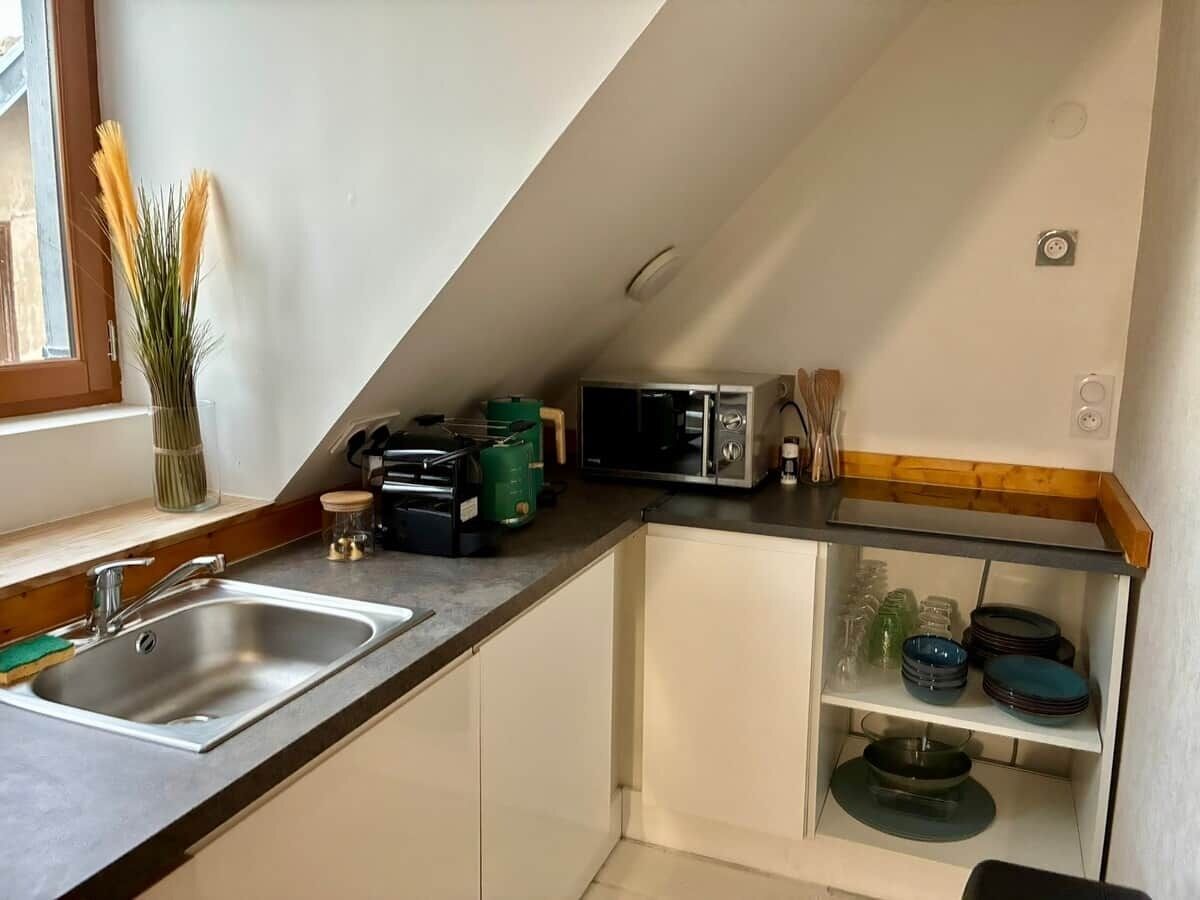 Uma cozinha compacta com pia, micro-ondas, torradeira e armário de vidro com louças.