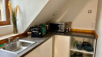 Uma cozinha compacta com pia, micro-ondas, torradeira e armário de vidro com louças.