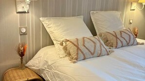 Et hotelværelse med en seng, to sengeborde med lamper, et natbord med en vase og en fletstol.