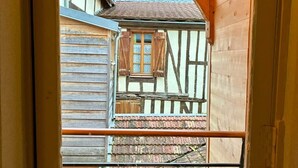 Una ventana con vista a una casa tradicional de entramado de madera, un alféizar de madera y tres objetos de cerámica blanca.