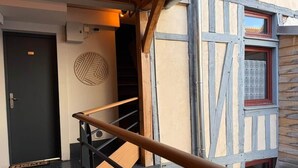 Una escalera conduce a un cuarto con una puerta oscura, un equipo de aire acondicionado instalado en la pared y un ventanal con marco rojo.