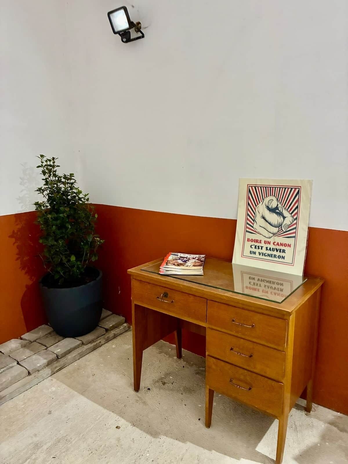 Een houten bureau met lades, een kamerplant en een poster.