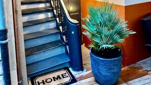 Eine Treppe mit hölzernem Geländer und einem schwarzen Schutzgeländer, die zu einem Raum führt, vor dem eine Fußmatte mit der Aufschrift 'HOME' liegt.