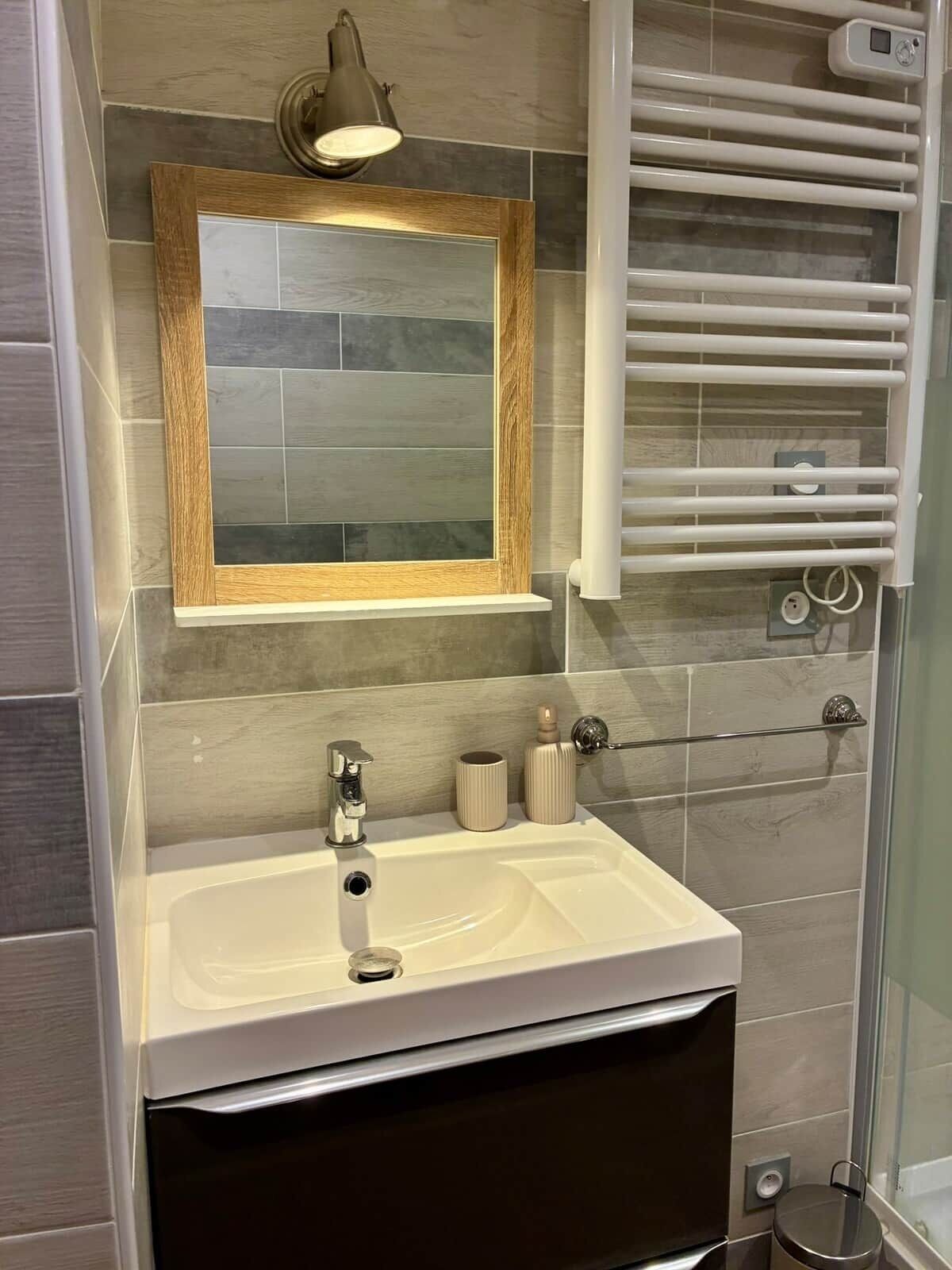 A bathroom with a wooden-framed mirror, a white sink, a towel rack, and a shower area.