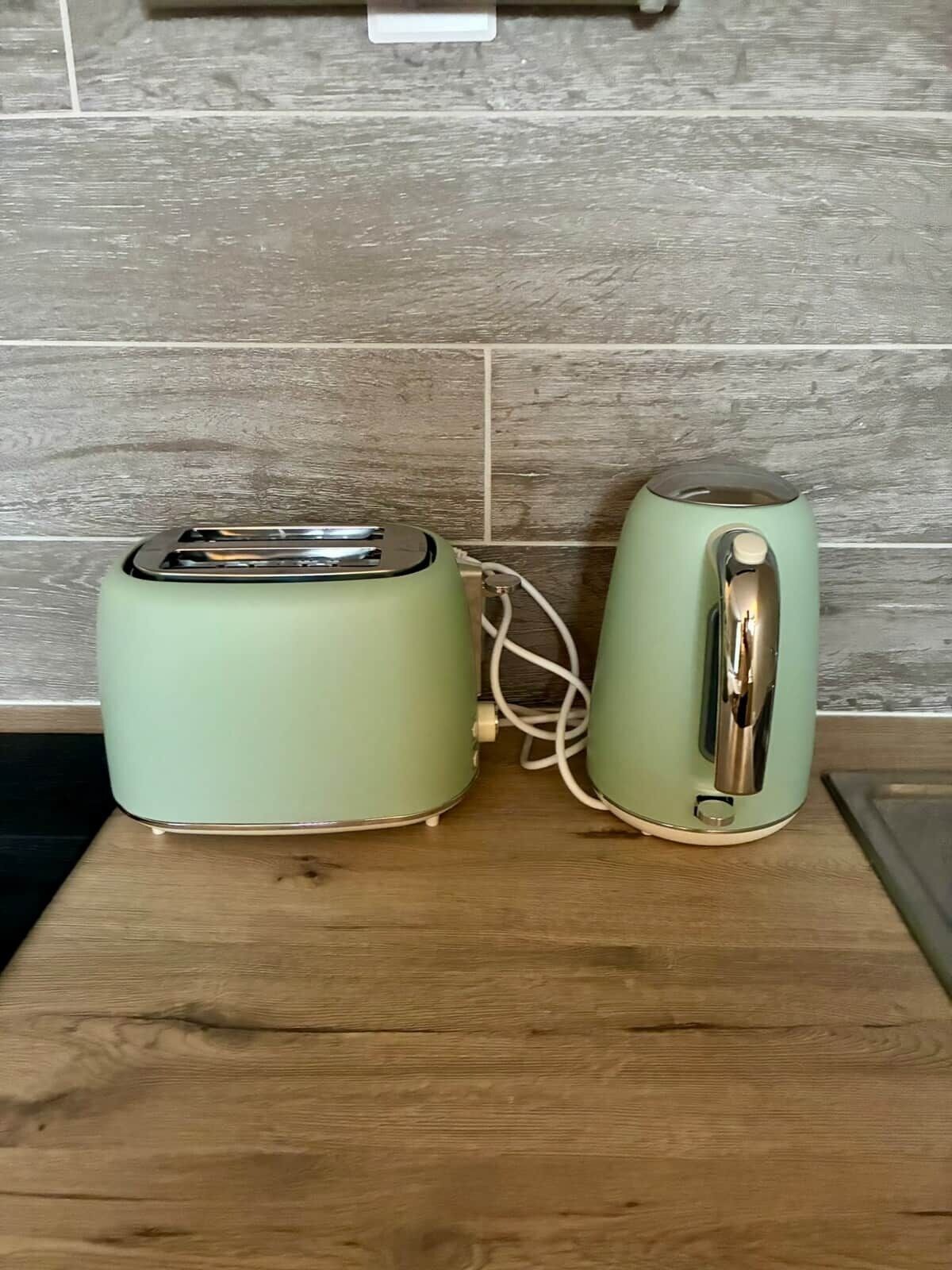 Deux appareils de cuisine, un grille-pain et une bouilloire, sont posés sur un plan de travail en bois, avec un pare-feu carrelé derrière.