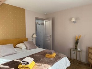 Ein Hotelzimmer mit Bett, Nachttisch, Lampe, Tür und einem kleinen Tisch mit einer Vase.