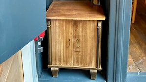 A wooden cabinet with two drawers and a shelf, a framed abstract artwork above it, and a vase with dried plants on the right. - La Grande Escapade (T12) (Troyes)