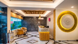 A reception area with a marble floor, a reception desk, a yellow chair, and a wall-mounted decorative piece. - Lords Inn Katra (Katra)