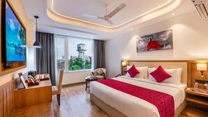 A hotel room with a bed, desk, TV, and a city view. - Lords Inn Katra (Katra)