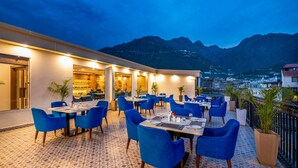 An outdoor dining area with blue chairs and tables, a patterned floor, and a mountain view in the background. - Lords Inn Katra (Katra)